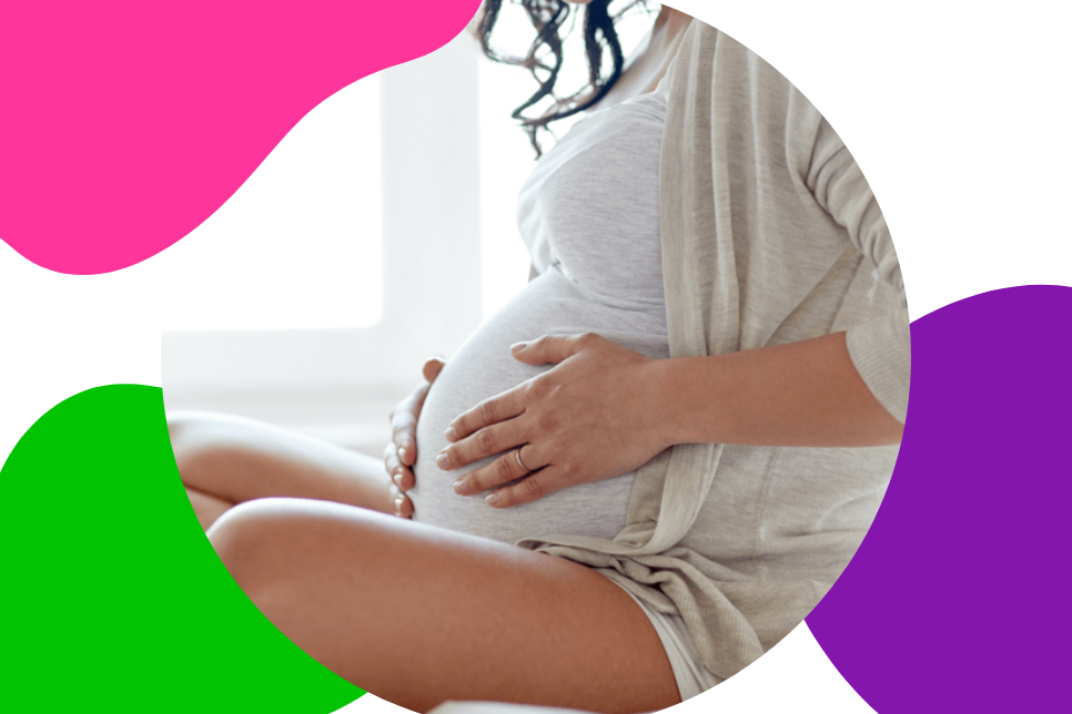 Frau mit fortgeschrittener Schwangerschaft sitz auf dem Bett und hält sich ihren Baby-Bauch