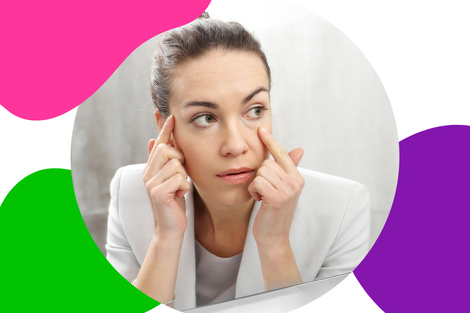 junge Frau mit braunen Haaren schaut sich im Spiegel ihre vergrößerten Augen an, welche ein Symptom von Morbus Basedow sind